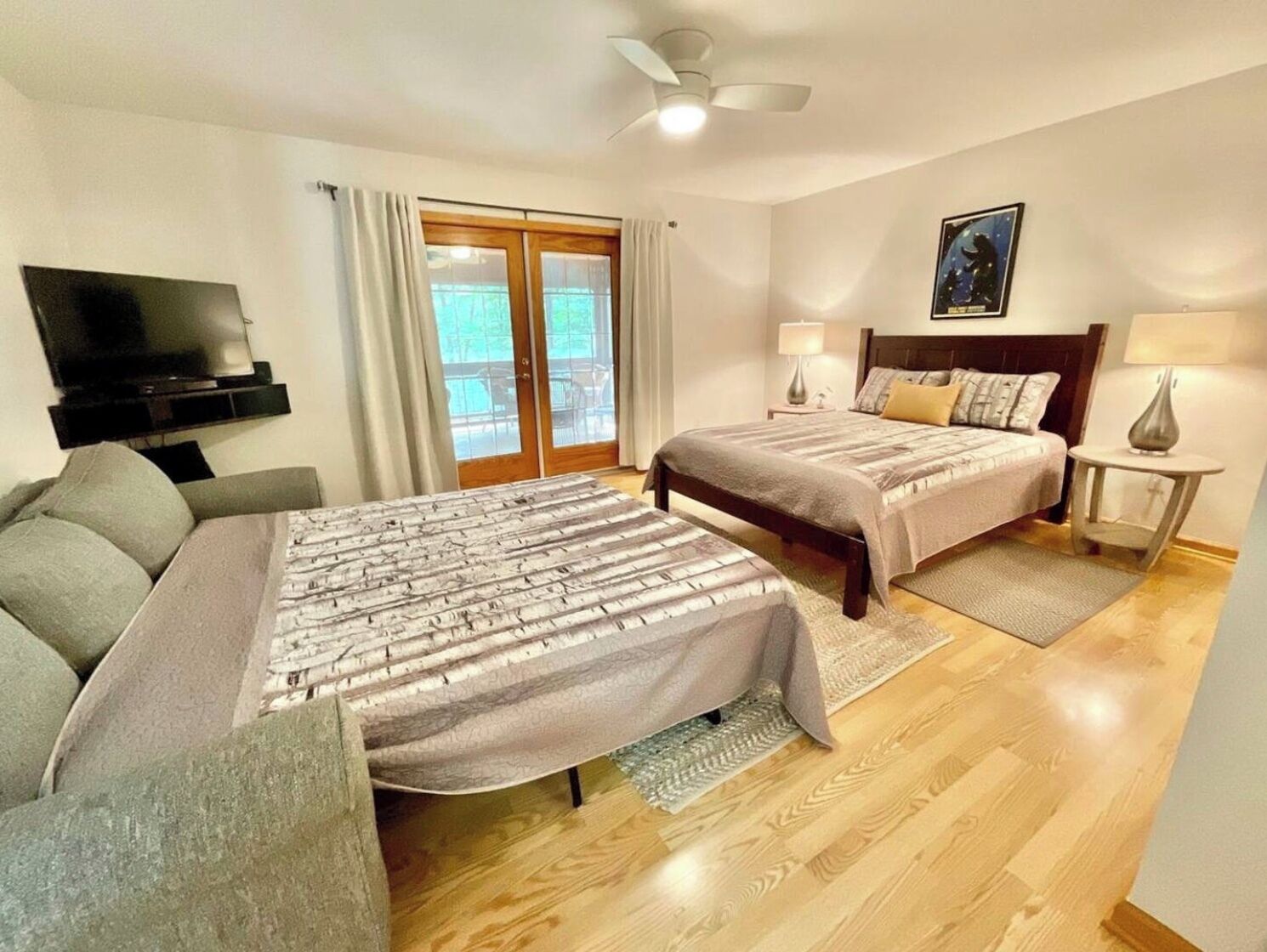 A hotel room with two beds, a TV, a balcony, and a ceiling fan.