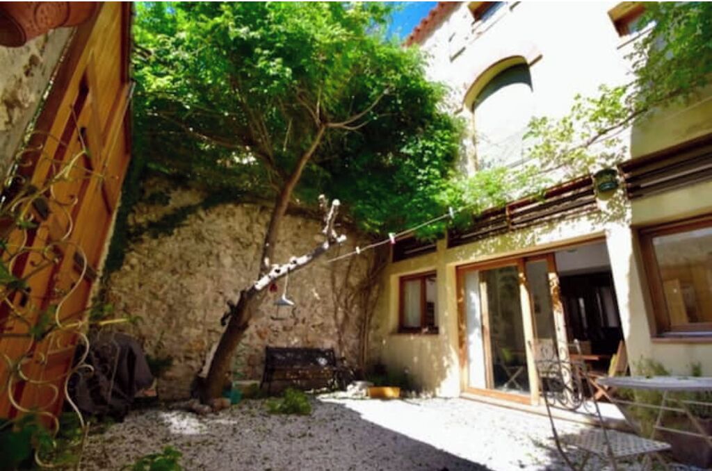 Une cour intérieure avec un mur en pierre, un arbre et un bâtiment doté de grandes fenêtres et d’un balcon.