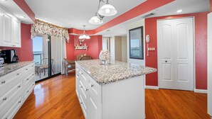 Une cuisine avec des meubles blancs, un plan de travail en granit et un mur d’accent rouge.