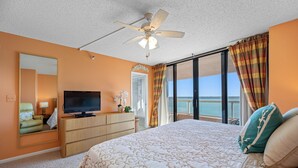 Une chambre d’hôtel avec un grand lit, une télévision, un ventilateur de plafond, une vue sur la mer et un balcon.