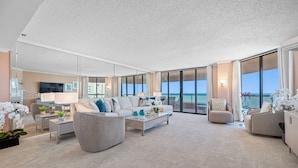 Un salon spacieux avec un grand canapé, une table basse et un téléviseur. Il y a un balcon avec vue sur l’océan.
