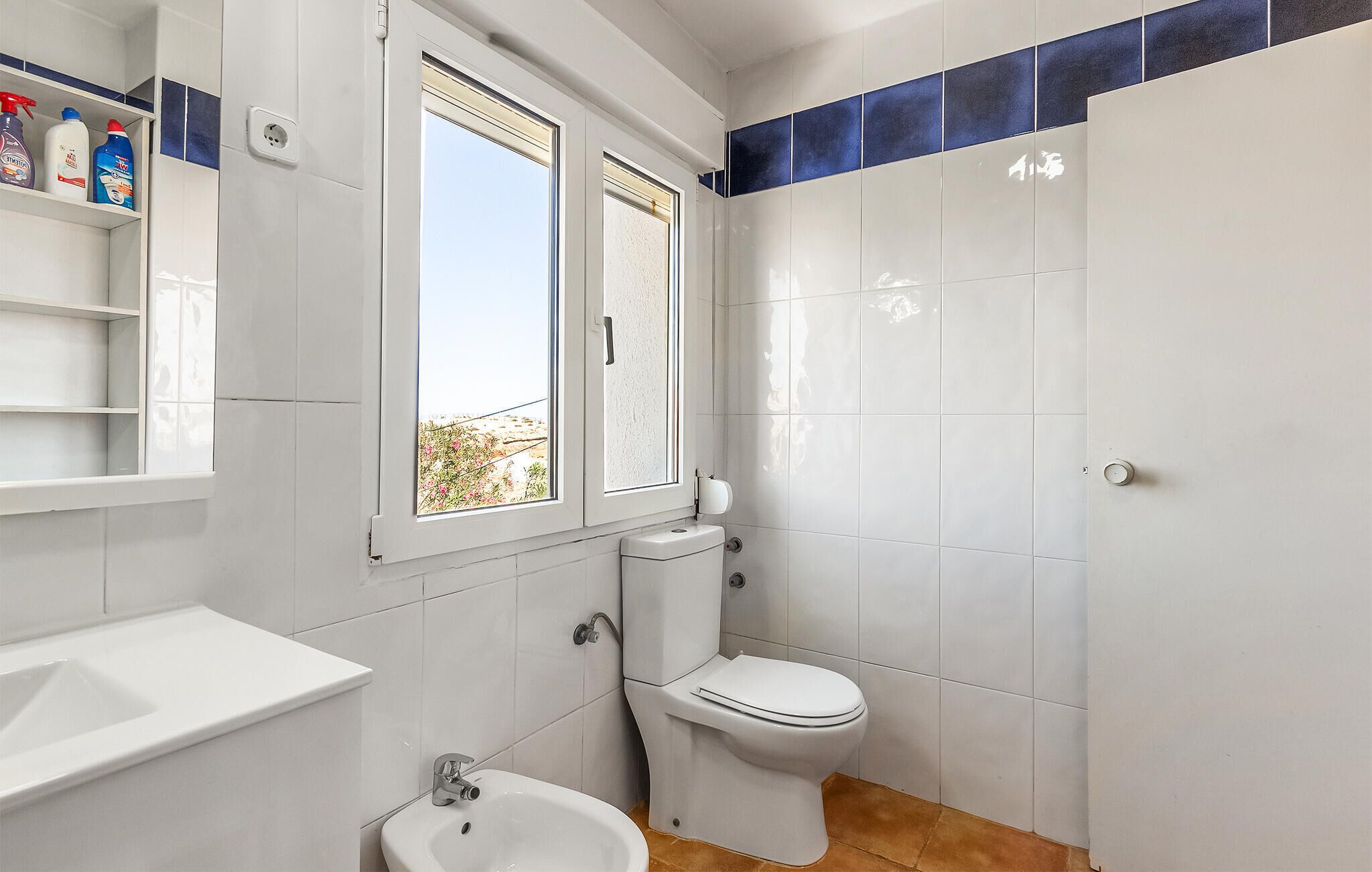 Ein Badezimmer mit Toilette, Bidet und Waschbecken. Ein Fenster bietet Blick auf Grünflächen.