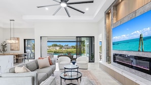 A modern living room with a large TV, comfortable seating, and a view of the ocean. - Peach Paradise: Luxury Saltwater Pool & Game Room (Cape Coral)