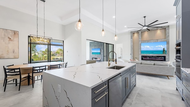 A modern kitchen with a large island, a dining area with a view, and a living space with a TV and fireplace. - Peach Paradise: Luxury Saltwater Pool & Game Room (Cape Coral)