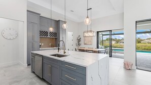 A modern kitchen with grey cabinets, a marble island, and pendant lighting. - Peach Paradise: Luxury Saltwater Pool & Game Room (Cape Coral)