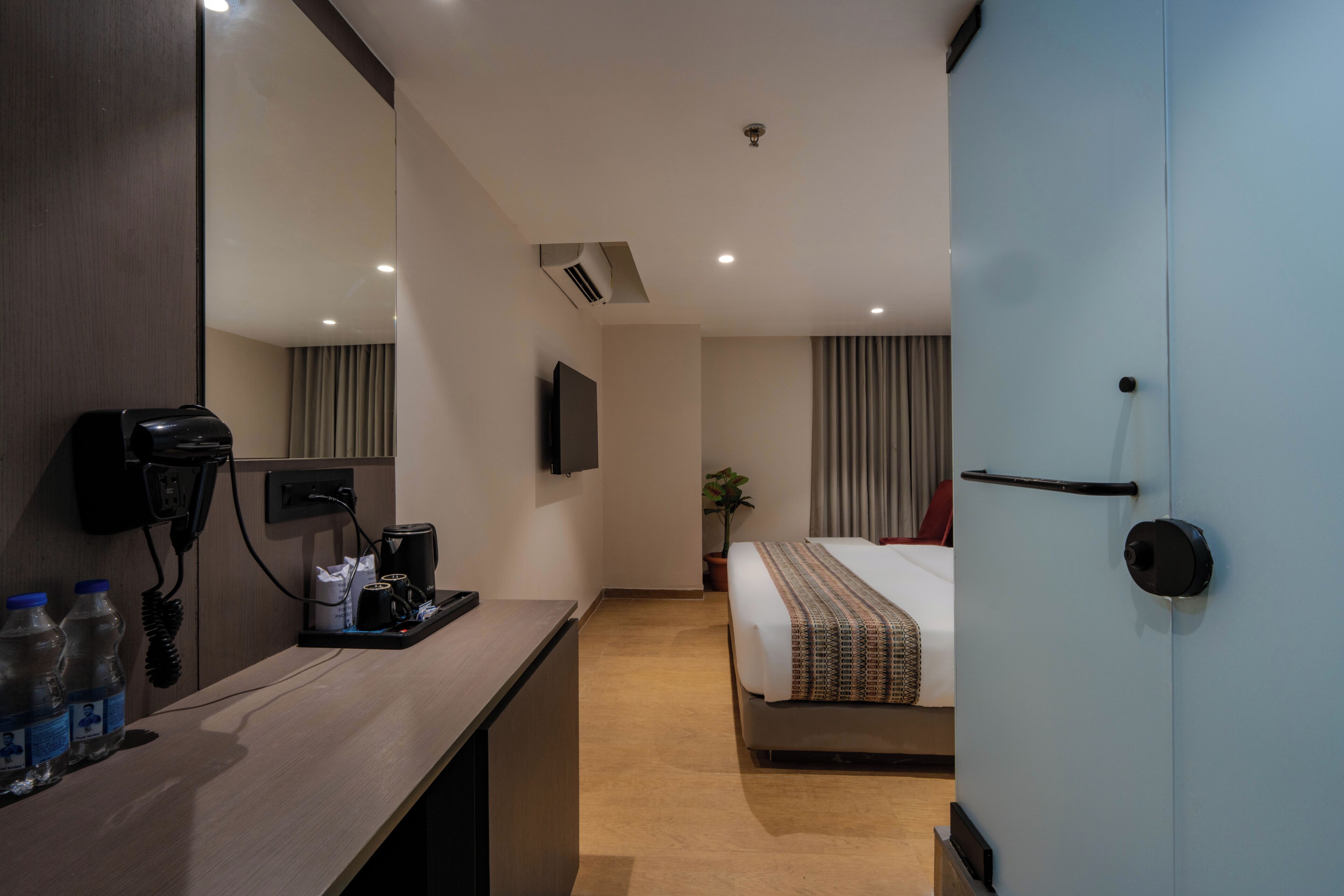 A hotel room with a desk, a bed, a TV, a door, and a window with curtains.