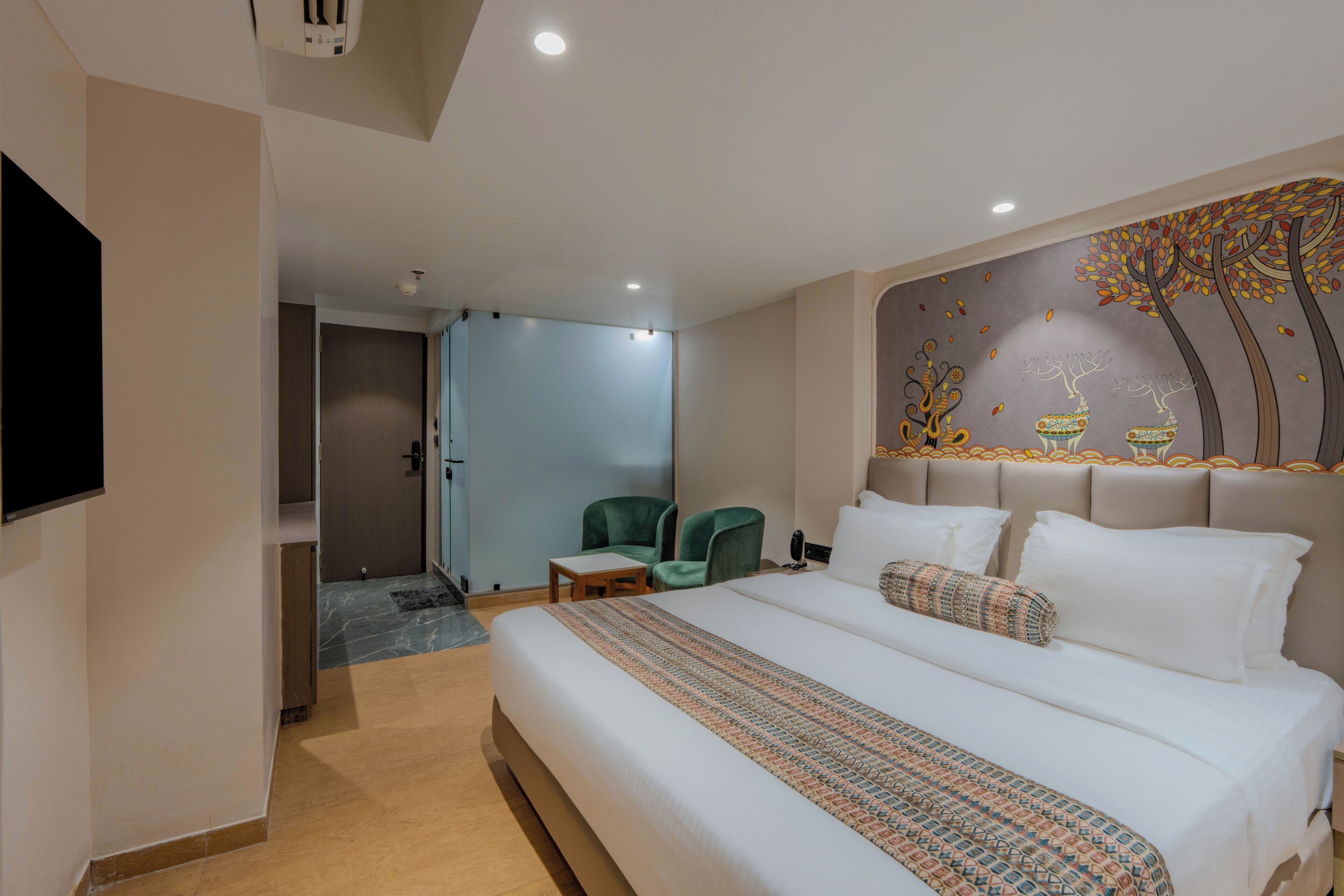 A hotel room with a large bed, a flat-screen TV, a wall-mounted artwork, and a seating area with chairs.