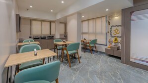 A modern dining area with tables and chairs, a kitchen in the background, and a decorative wall with an emblem.