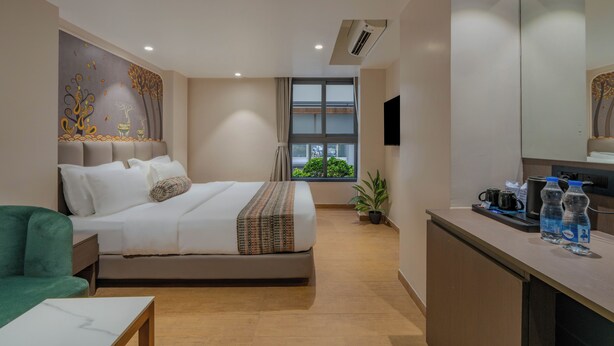 A hotel room with a bed, a desk, a chair, a potted plant, and a window with a view.