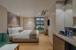 Habitación de hotel con cama, escritorio, silla, planta en maceta y ventana con vista.