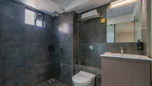 A modern bathroom with dark tiles, a shower, a toilet, a sink, and a mirror.