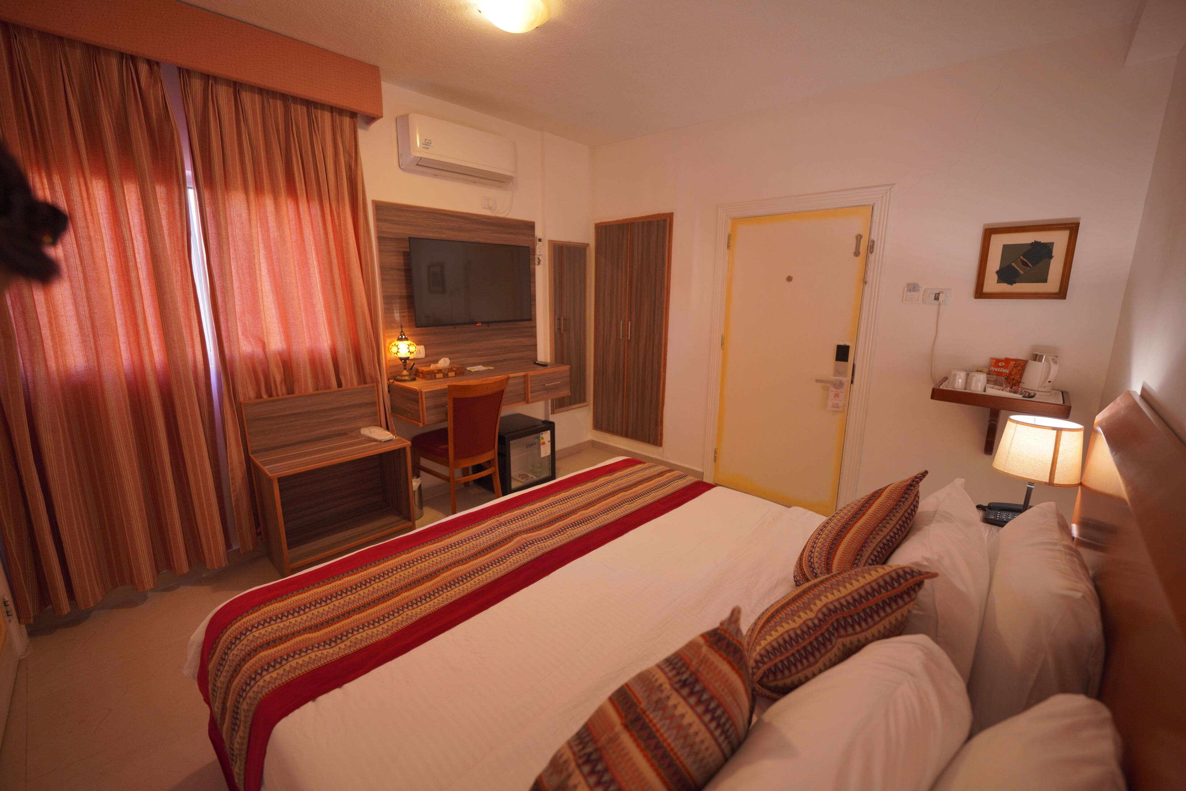 Una habitación de hotel con cama, escritorio, silla, televisor y puerta.