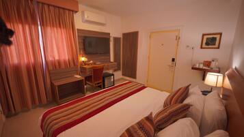 Una habitación de hotel con cama, escritorio, silla, televisor y puerta.