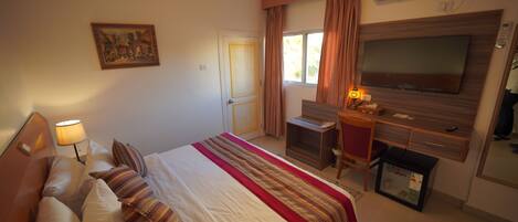 A hotel room with a bed, a desk, a television, and an air conditioning unit.