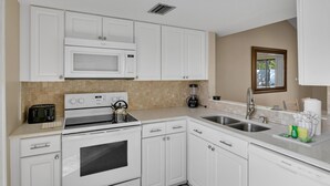 Una cocina con gabinetes blancos, microondas, estufa, pileta y ventana con vista.