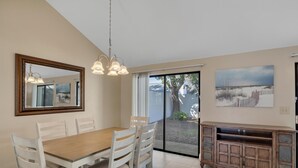 Un comedor con mesa y sillas de madera, un espejo grande y un puerta corrediza de vidrio que da a un espacio al aire libre.