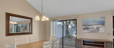 A dining area with a wooden table and chairs, a large mirror, and a sliding glass door leading to an outdoor area.