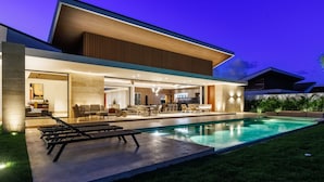 Ein modernes Haus mit Swimmingpool, Sitzgelegenheiten im Freien und einem gut beleuchteten Innenraum.