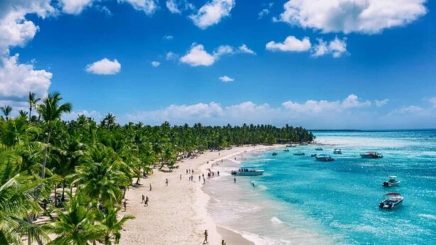 Ein Strand mit klarem türkisblauem Wasser, Palmen und Booten.