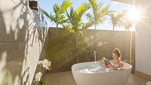 Eine Frau entspannt in einer großen Badewanne mit einem Buch, umgeben von Pflanzen in einem sonnendurchfluteten Raum.