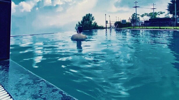 A swimming pool with a person in the water, surrounded by a fence and trees.