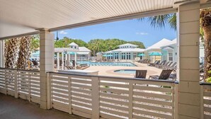 Ein überdachter Poolbereich mit Liegestühlen und Sonnenschirmen, ein Schwimmbecken und Gebäude im Hintergrund.