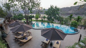 A pool area with lounge chairs and umbrellas, surrounded by trees and a view of a river. - Toyam by Orchid Hotels (Bhor)