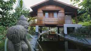 A wooden house with a balcony, surrounded by lush greenery and a water feature. - Toyam by Orchid Hotels (Bhor)