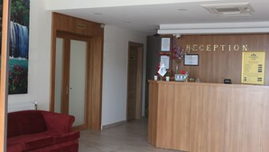 A reception area with a wooden reception desk, a red sofa, and a framed painting of a waterfall. - Longoz Hotel (Demirköy)