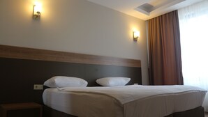 A hotel room with a bed, two wall-mounted lights, a window with curtains, and a wooden headboard. - Longoz Hotel (Demirköy)