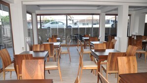 A spacious dining area with wooden tables and chairs, large windows with a view of parked cars and buildings outside. - Longoz Hotel (Demirköy)