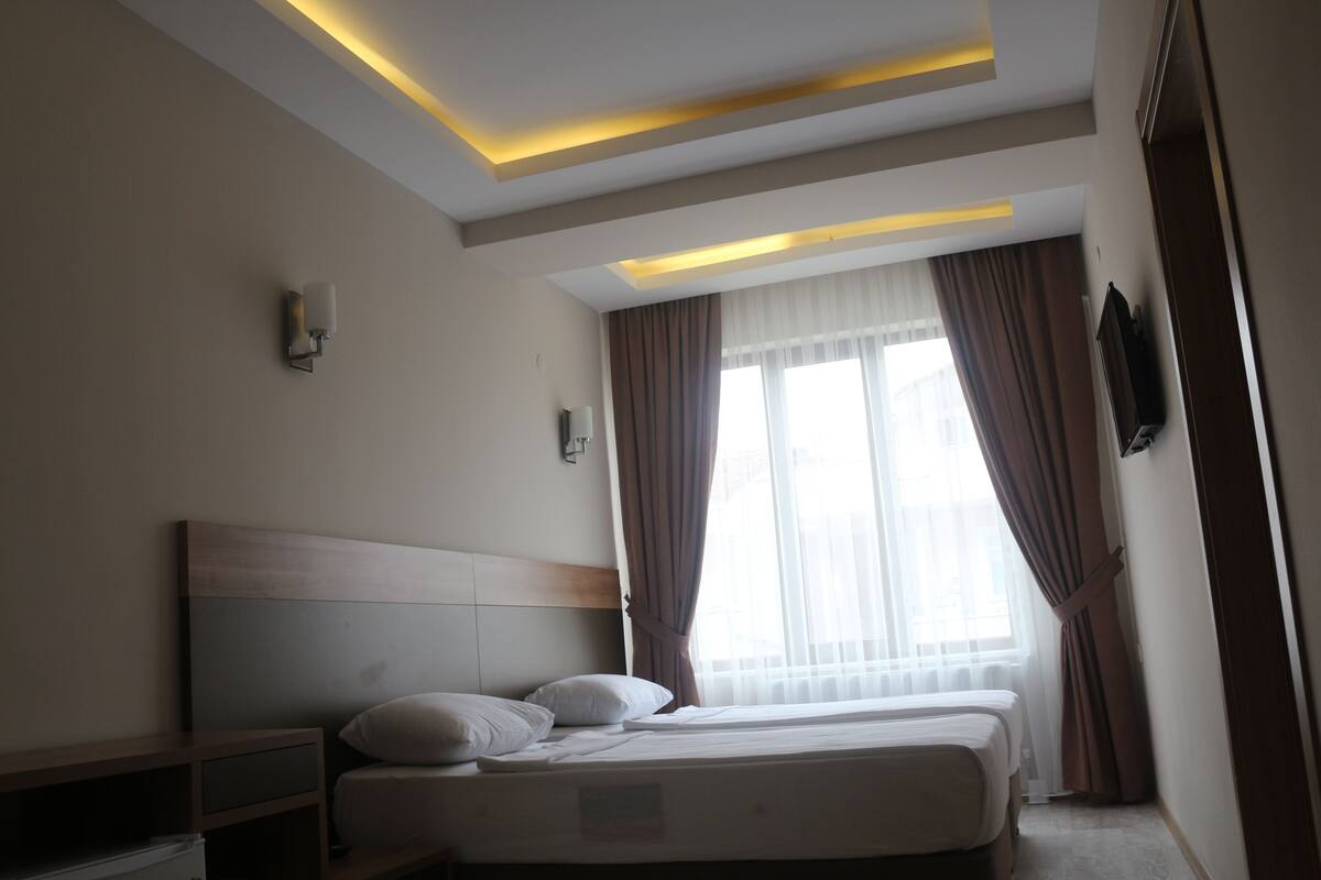 A hotel room with a large bed, bedside tables, a flat-screen TV, and a window with curtains.