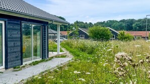 A modern building with large glass windows and a pathway leading to a garden area with various plants and flowers.