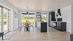 A modern kitchen with a central island, a dining area with a table and chairs, and a view of a garden through large windows.