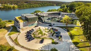 A modern hotel with a glass facade, a parking lot, and a view of a lake. - Hotel GLAR Conference & SPA (gmina Wolin)