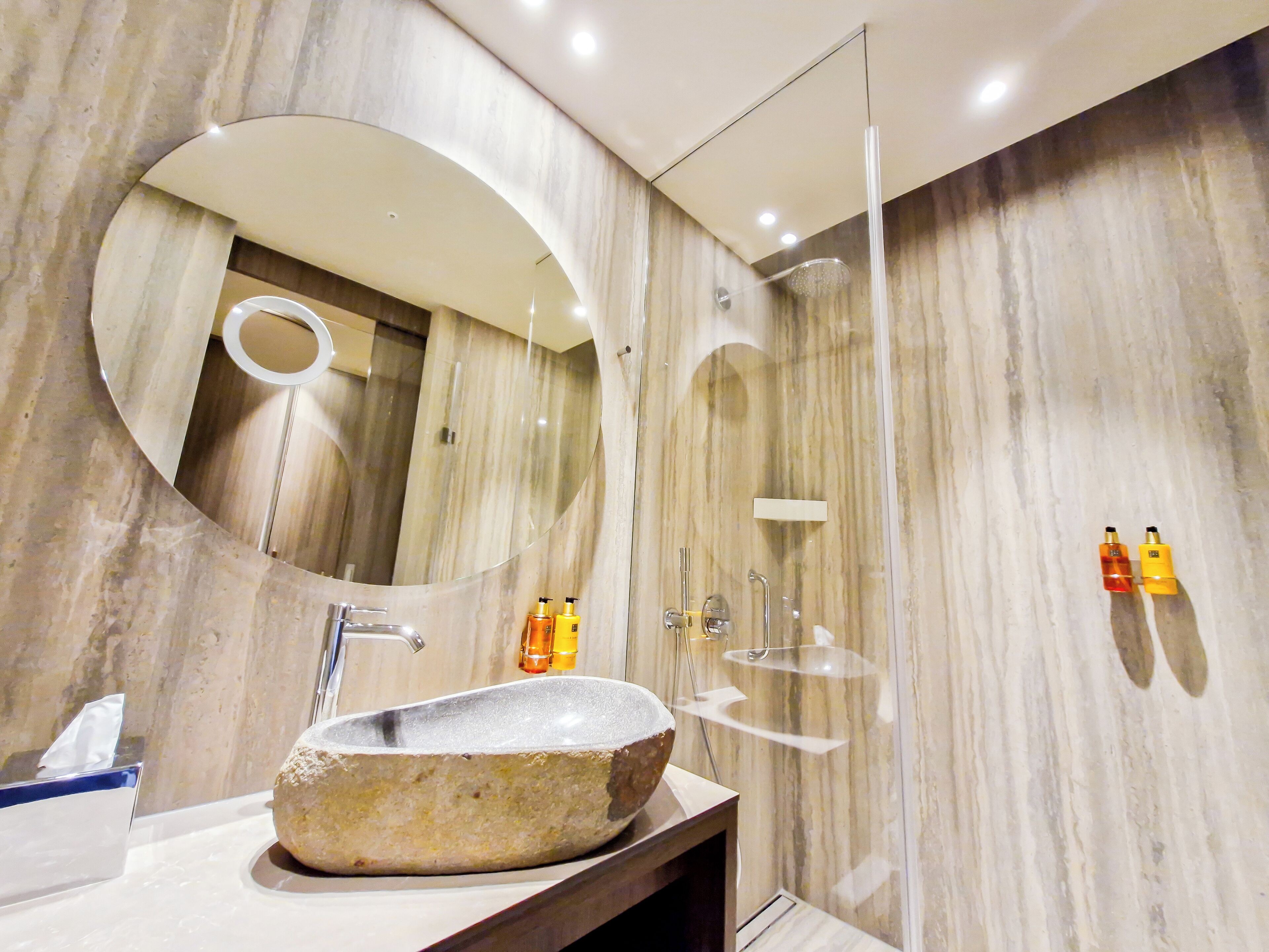 Une salle de bain moderne avec un lavabo en pierre, un miroir rond et une douche à parois de verre.