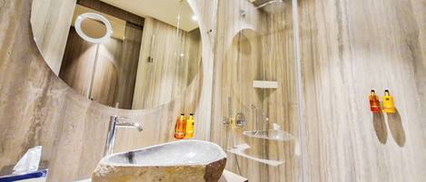 Une salle de bain moderne avec un lavabo en pierre, un miroir rond et une douche à parois de verre.