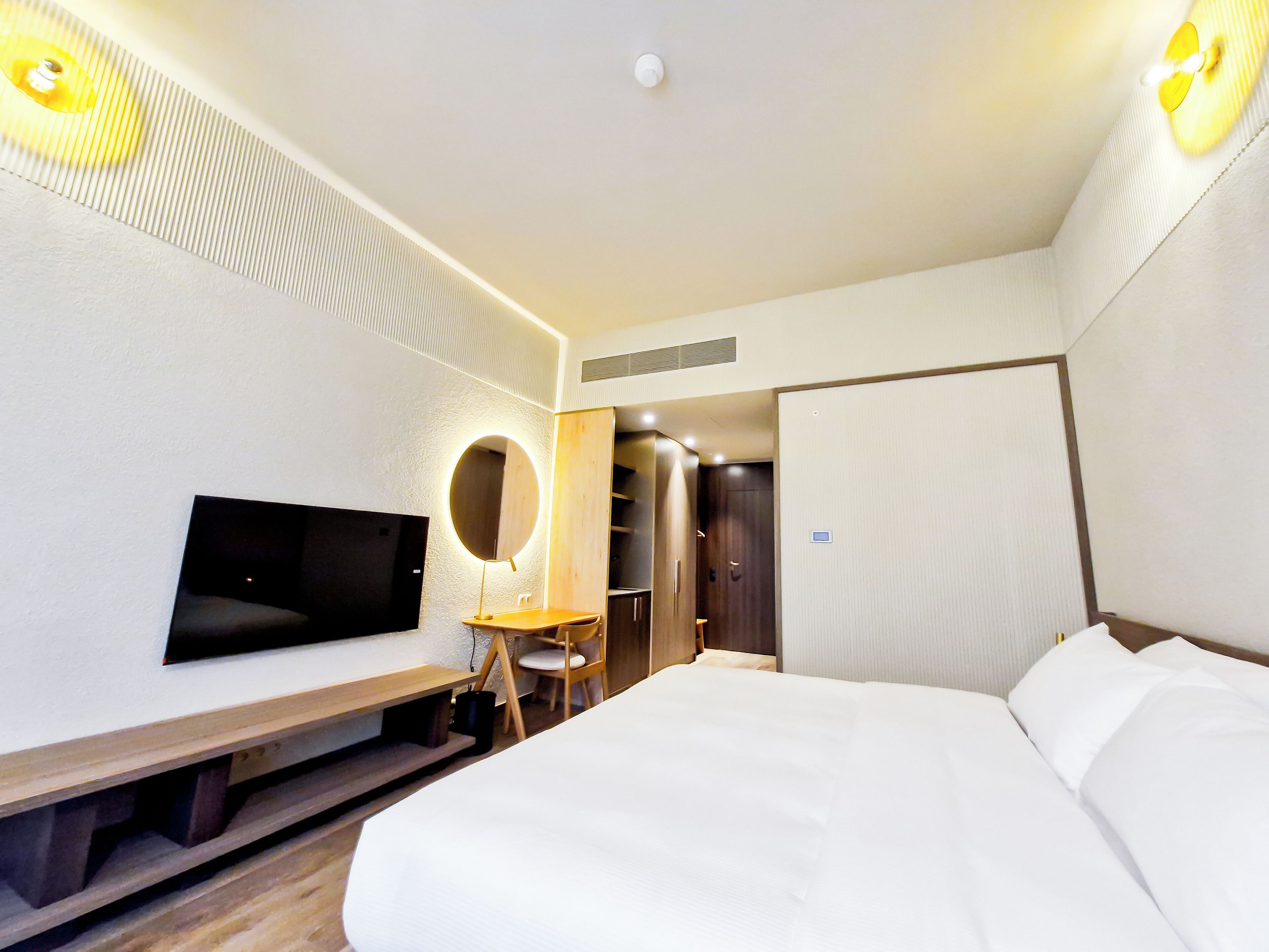 A hotel room with a bed, a TV, a bedside table, a mirror, and a wardrobe.