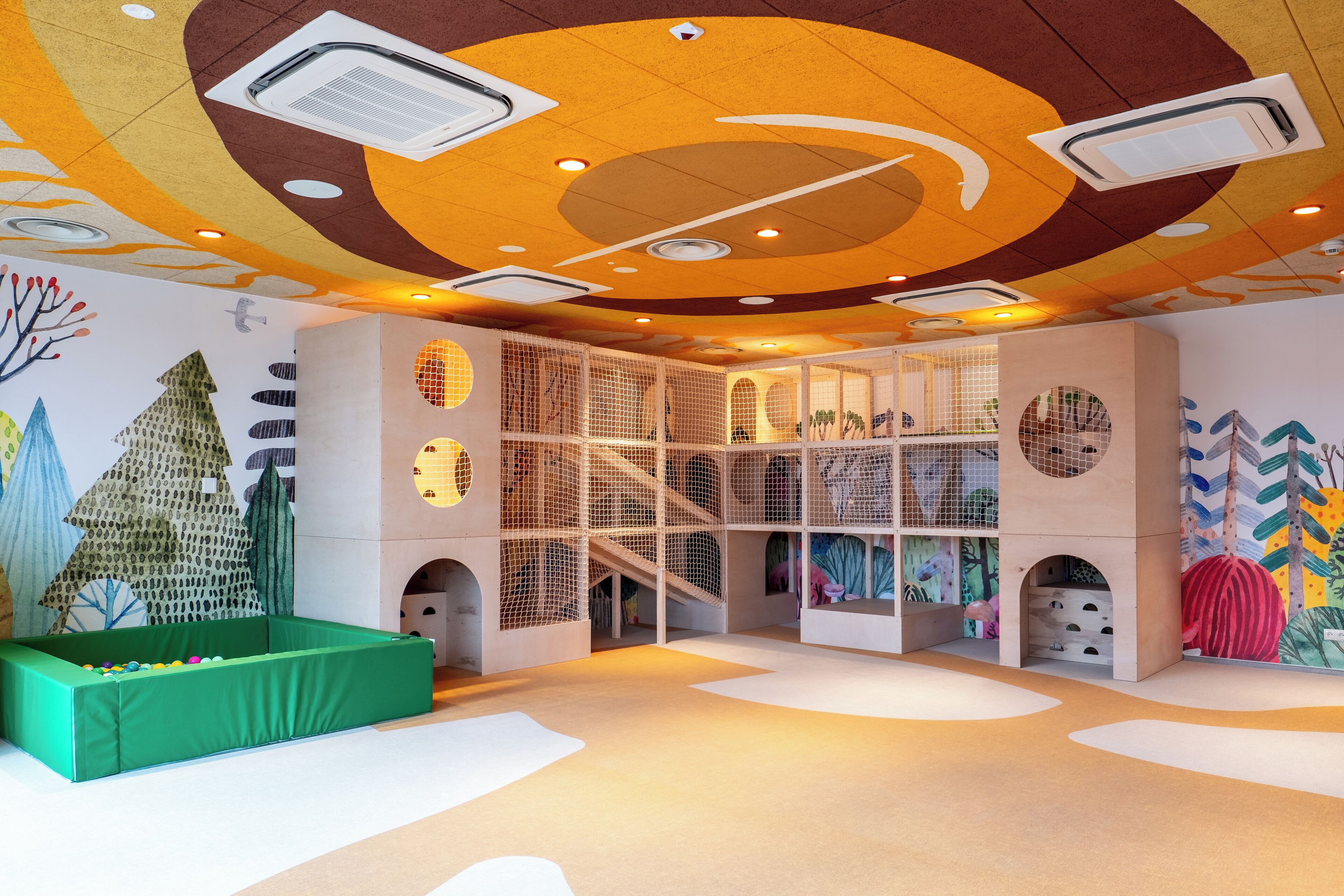 Uma área de recreação com cercado verde, estruturas de escalada com redes e murais coloridos.