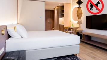 A hotel room with a bed, a TV, a desk, and a no-pet sign.