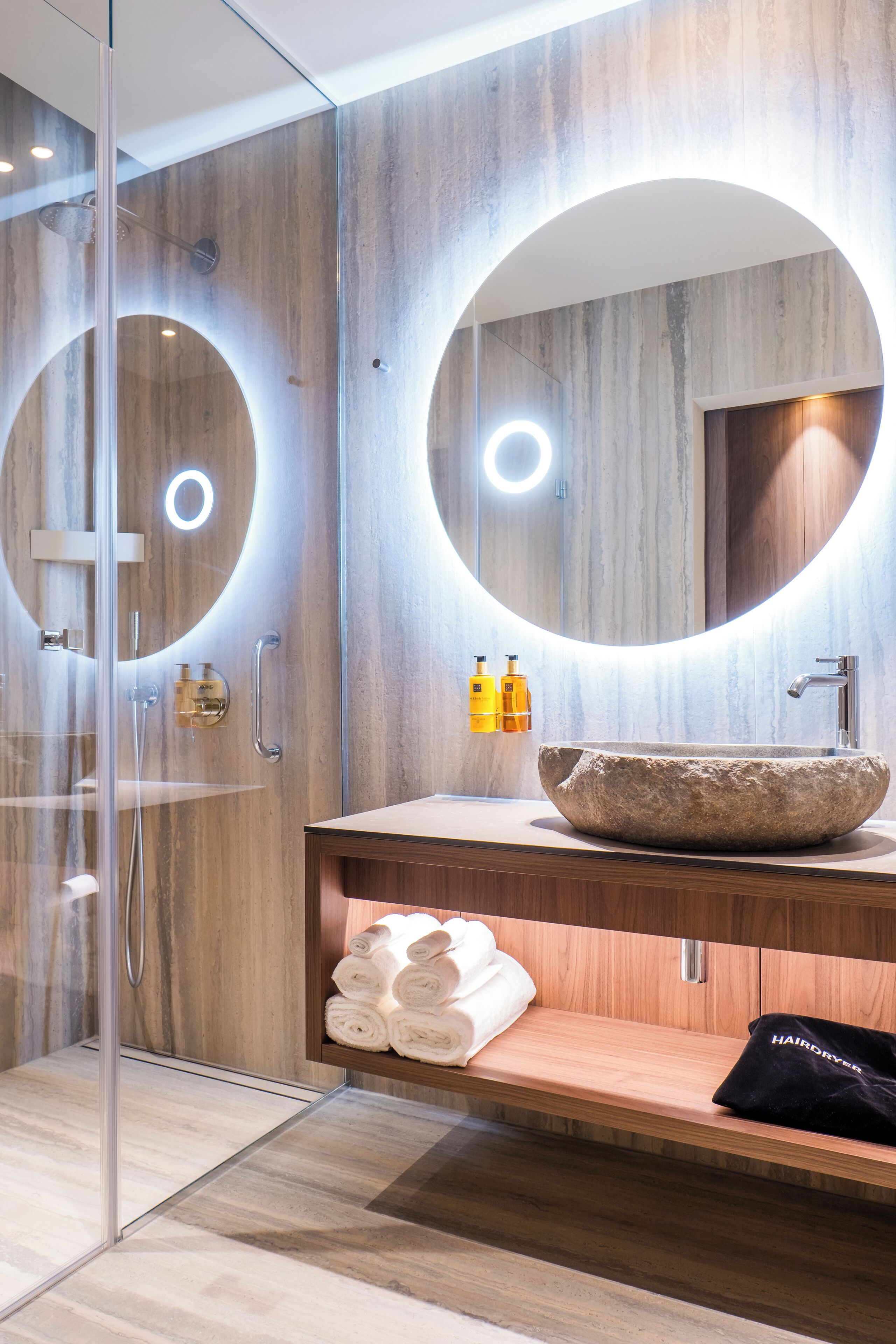A modern bathroom with a stone sink, wooden vanity, and a glass-enclosed shower.