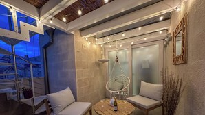 Un coin salon accueillant avec deux fauteuils confortables, un fauteuil suspendu et une table ronde en bois sur laquelle se trouvent une bouteille et des verres.