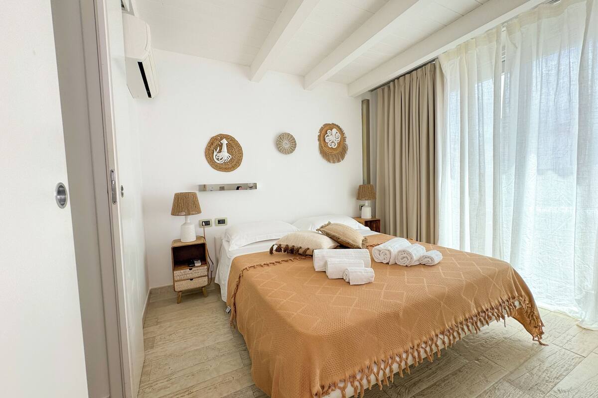 Een goed verlichte slaapkamer met een bed, nachtkastjes en een raam met gordijnen.