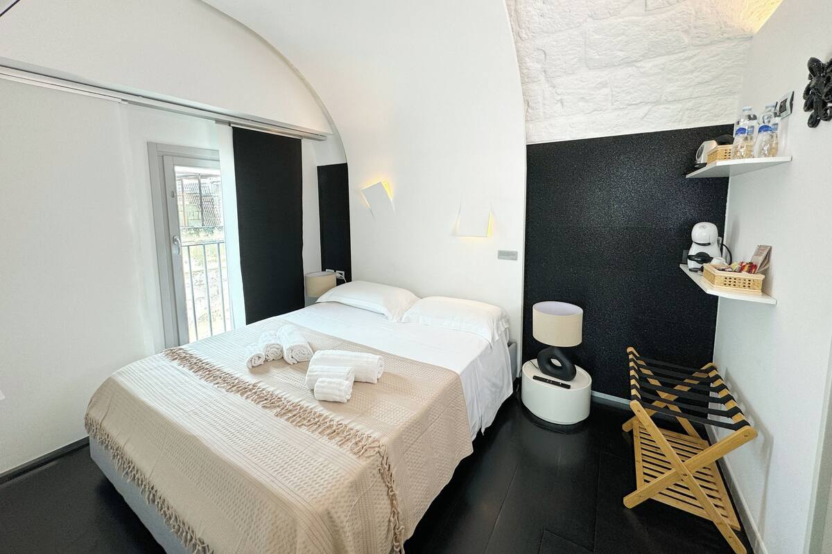 Een moderne hotelkamer met een groot bed, een klein bureau, een stoel, een lamp en een plankje met toiletartikelen.