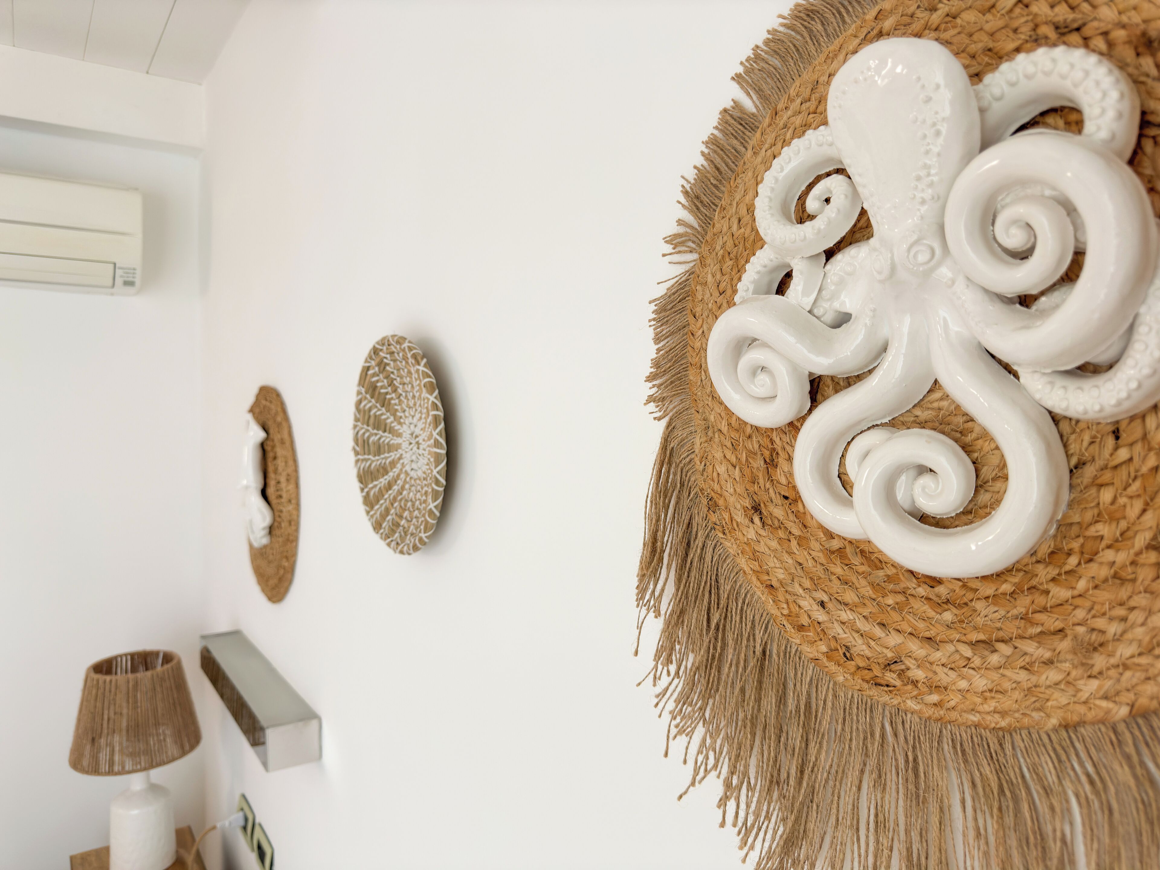 A room with a woven wall hanging, a white air conditioning unit, and a lamp on a wooden table.