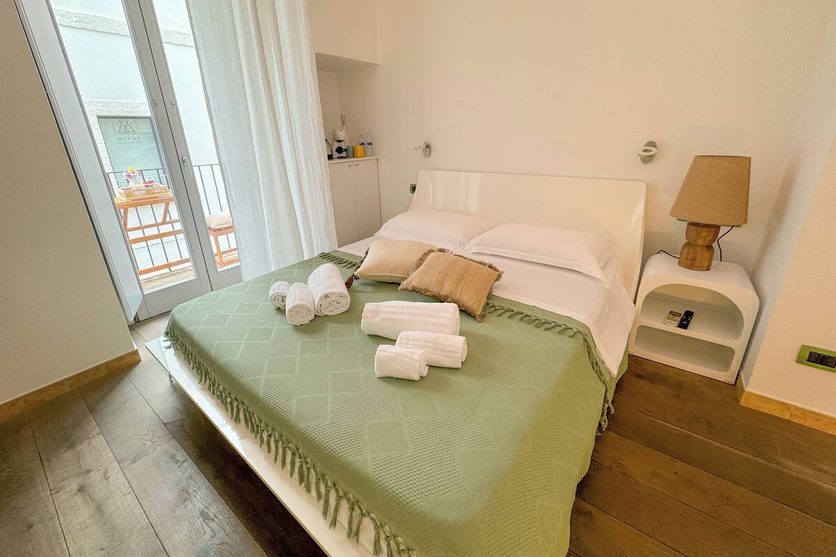 Een hotelkamer met een bed, een nachtkastje, een lamp en uitzicht op het balkon.