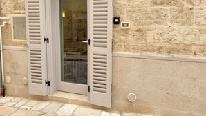 Une porte avec des volets, un mur de pierre et une petite fenêtre dotée d’une grille d’aération.