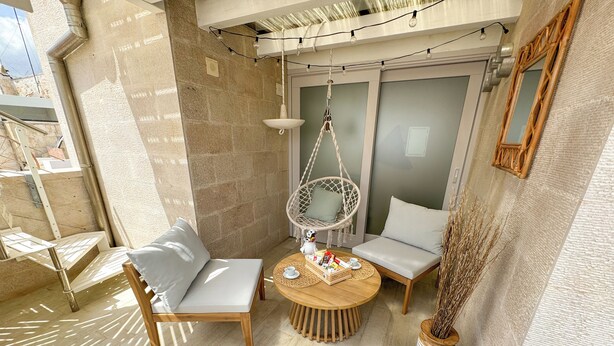Un espace de détente extérieur accueillant, avec une table ronde en bois, deux fauteuils rembourrés, un fauteuil suspendu et une plante en pot.