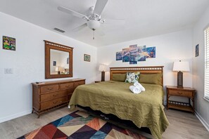 A bedroom with a bed, a ceiling fan, a dresser, a mirror, and wall art.