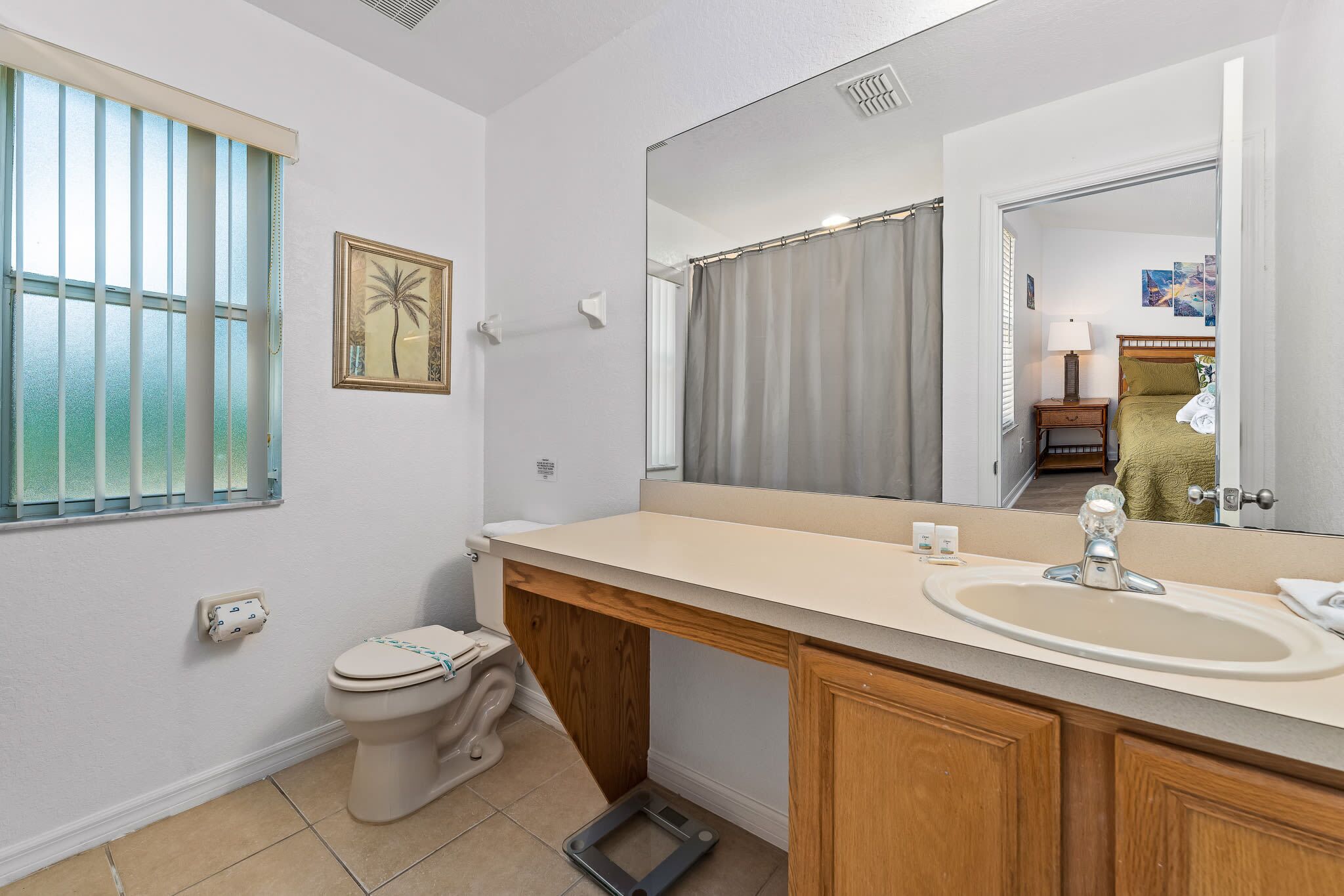 Ein Badezimmer mit Toilette, Waschbecken, Spiegel und einem Fenster mit Jalousien.